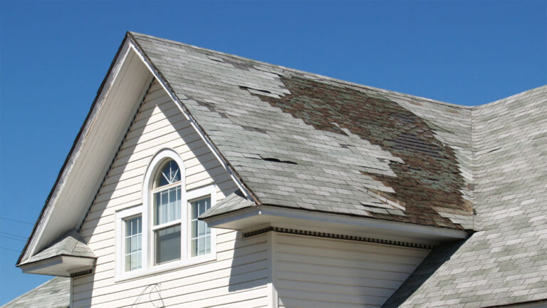 A white house with water damage in a large dark patch on the top of its roof