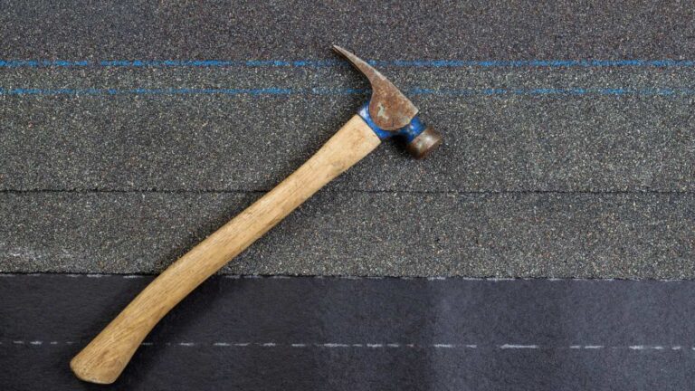 A hammer rests on top of asphalt roofing material.