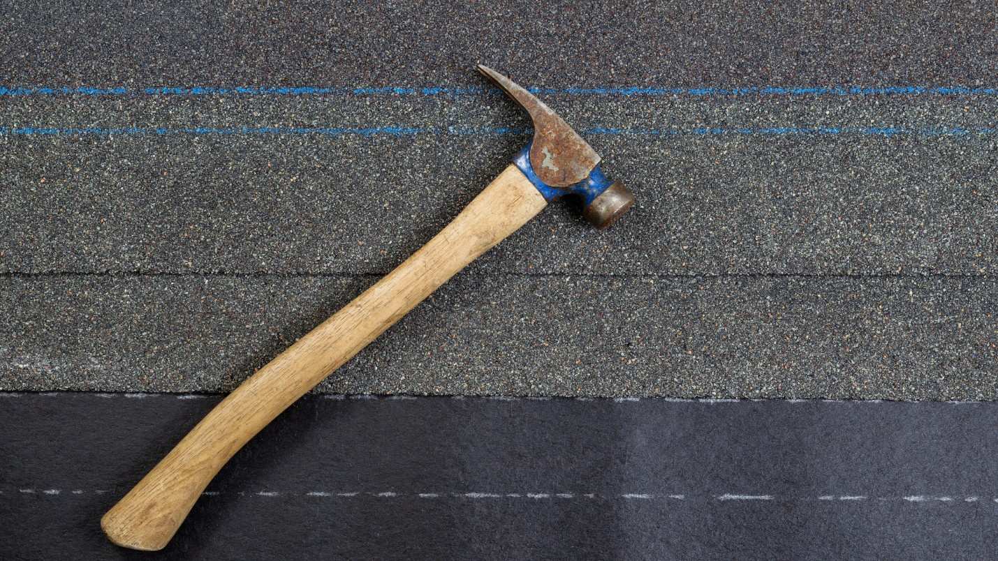 A hammer rests on top of asphalt roofing material.